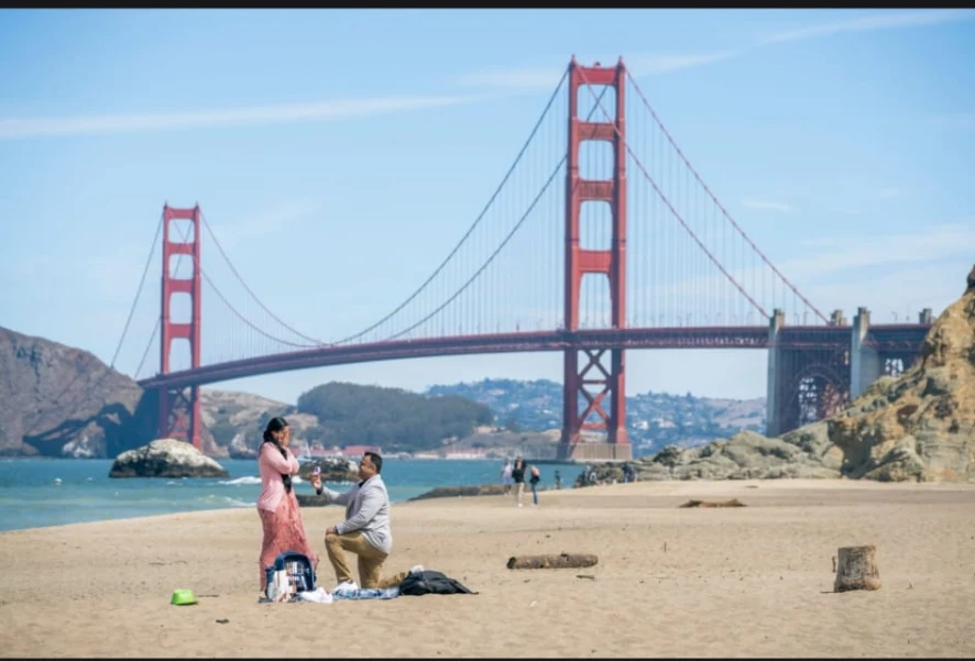 Samir proposing to Margarita on Baker Beach with the Golden Gate Bridge behind them